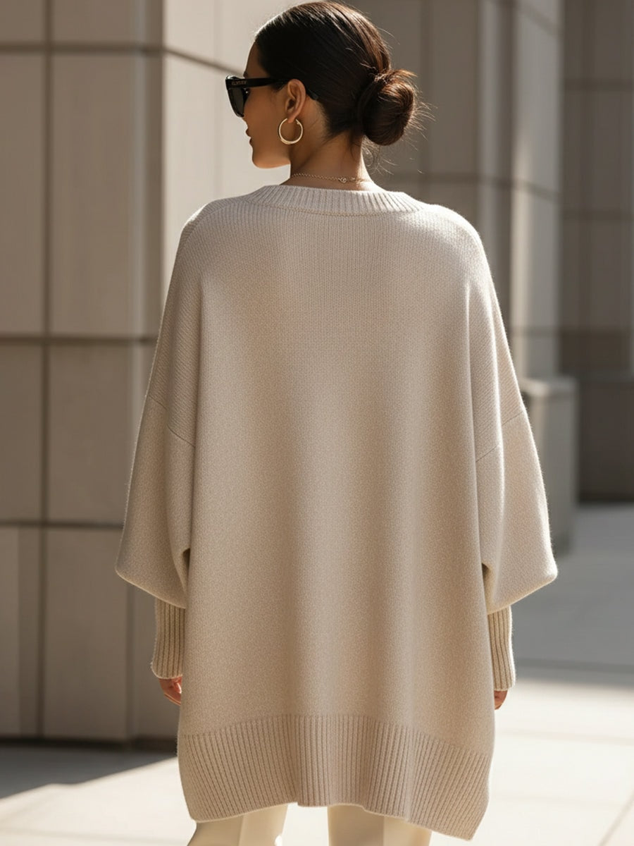 Back view of the cream longline poncho sweater, showing its relaxed drape, wide sleeves, and ribbed lower hem.