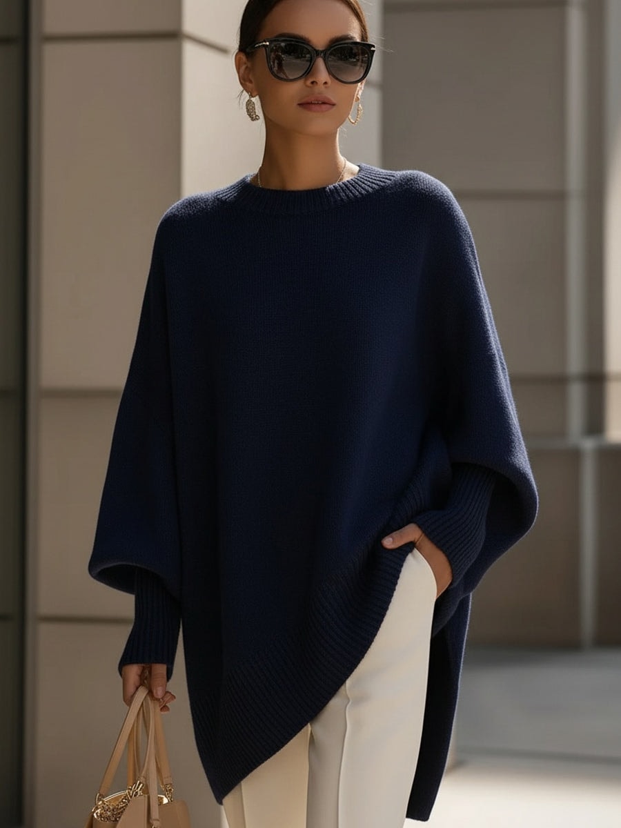 Navy asymmetric poncho sweater with a crew neckline, relaxed batwing sleeves, and ribbed trim worn with light trousers.