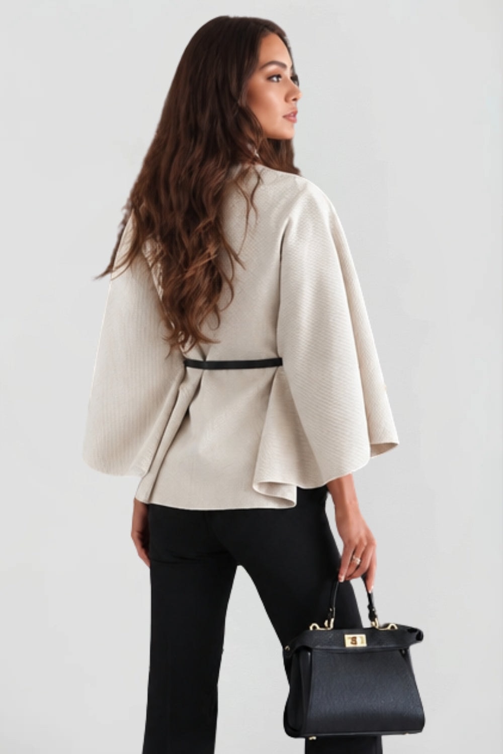Back three-quarter view of the cream belted cape jacket, showing the gathered waist and fluid sleeve shape.