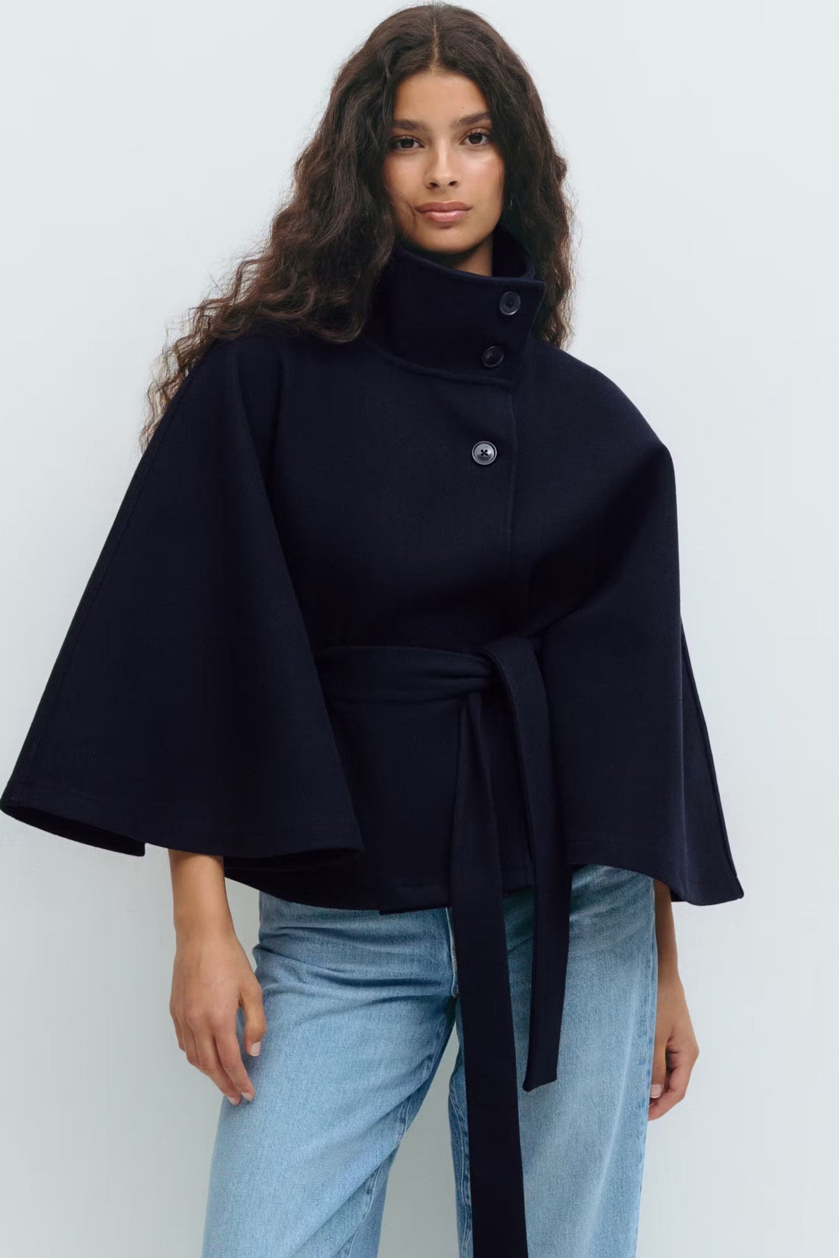 Navy cape jacket worn with the stand collar raised, button closure fastened, and belt tied at the waist.