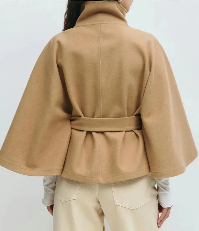 Back view of the camel cape coat showing the high collar, center-back seam, wide sleeves, and belt cinched at the waist.