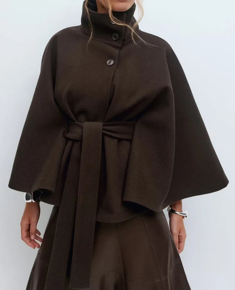 Dark brown belted cape coat paired with a matching skirt, highlighting the structured high neckline and broad draped sleeves.