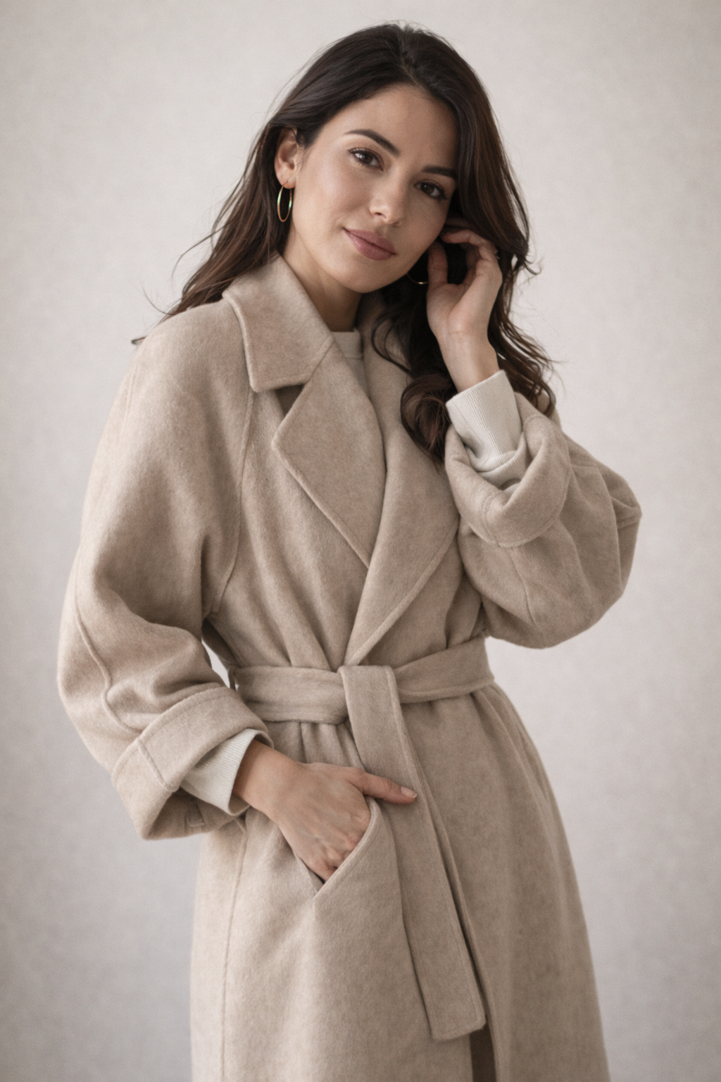 Close view of a model in a light taupe wrap coat, showing the wide lapel collar, tied belt, and front pocket.