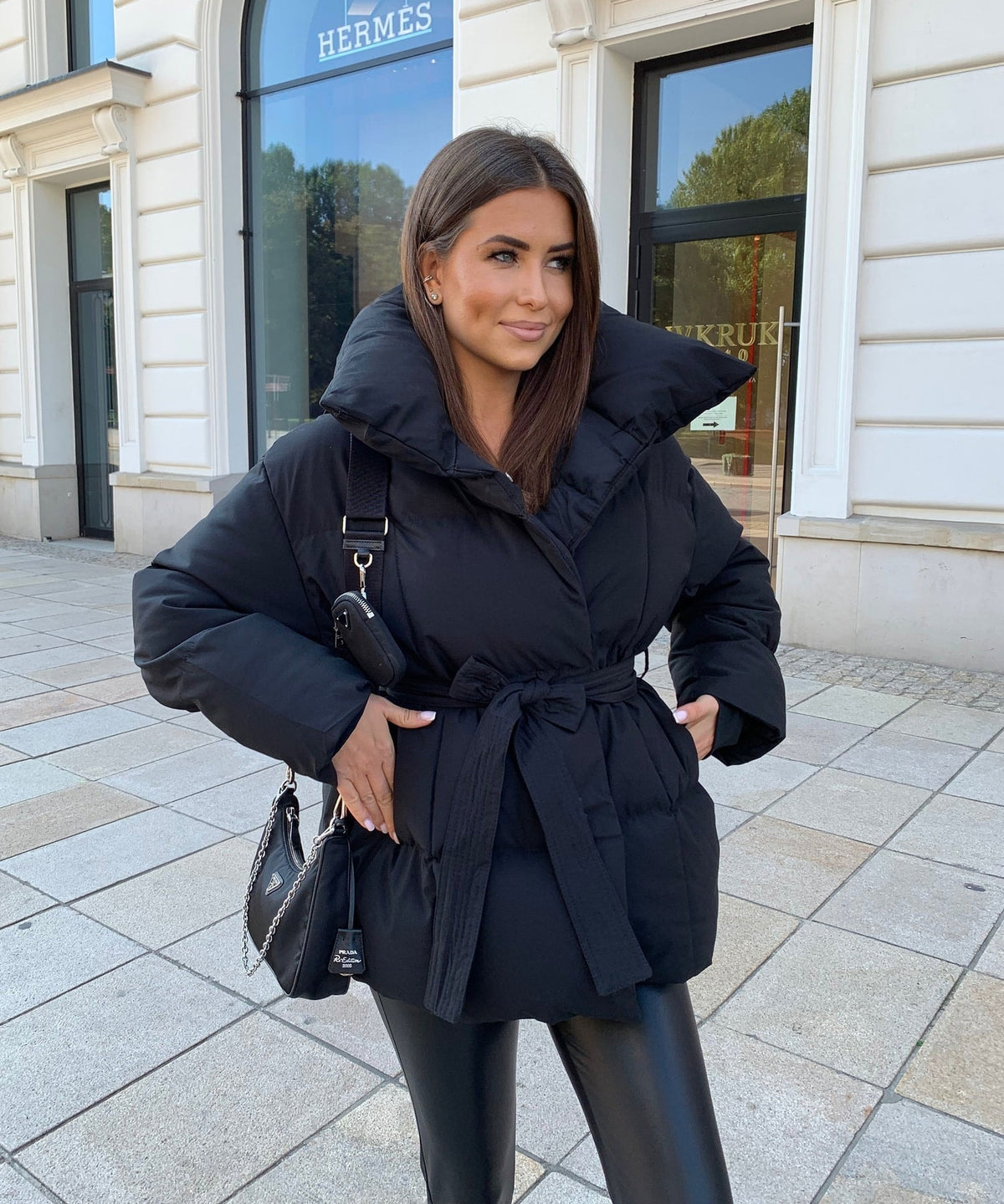 Black belted puffer jacket shown from the front with the waist tie wrapped and knotted over the padded body.
