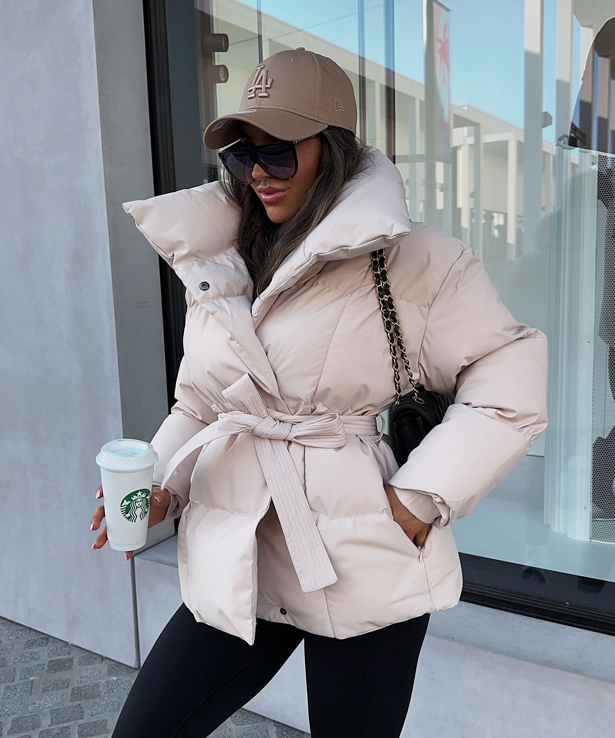 Light beige puffer jacket styled with the waist tie knotted at the front and hands tucked into the side pockets.