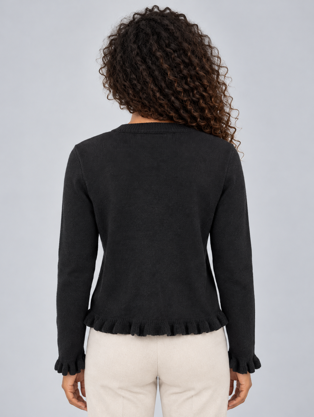 Back view of the black waist-length cardigan, showing its smooth back and ruffled hem and sleeve cuffs.