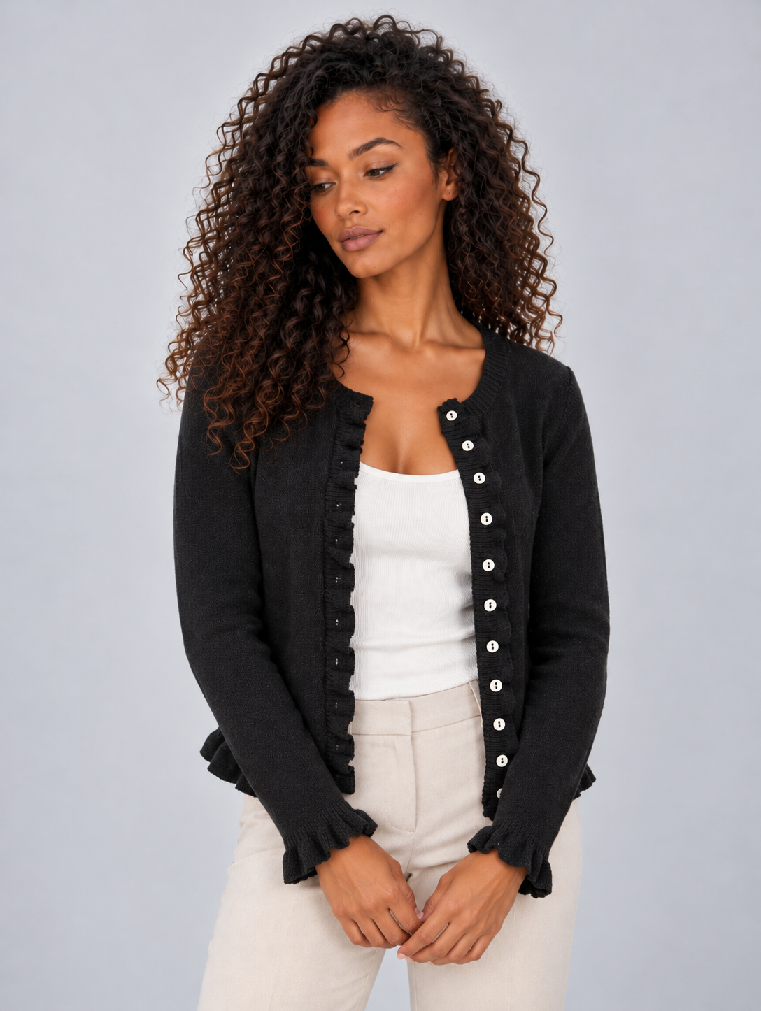 Black cardigan worn open over a white top, highlighting the full button-front edges, fitted sleeves, and ruffle detailing.