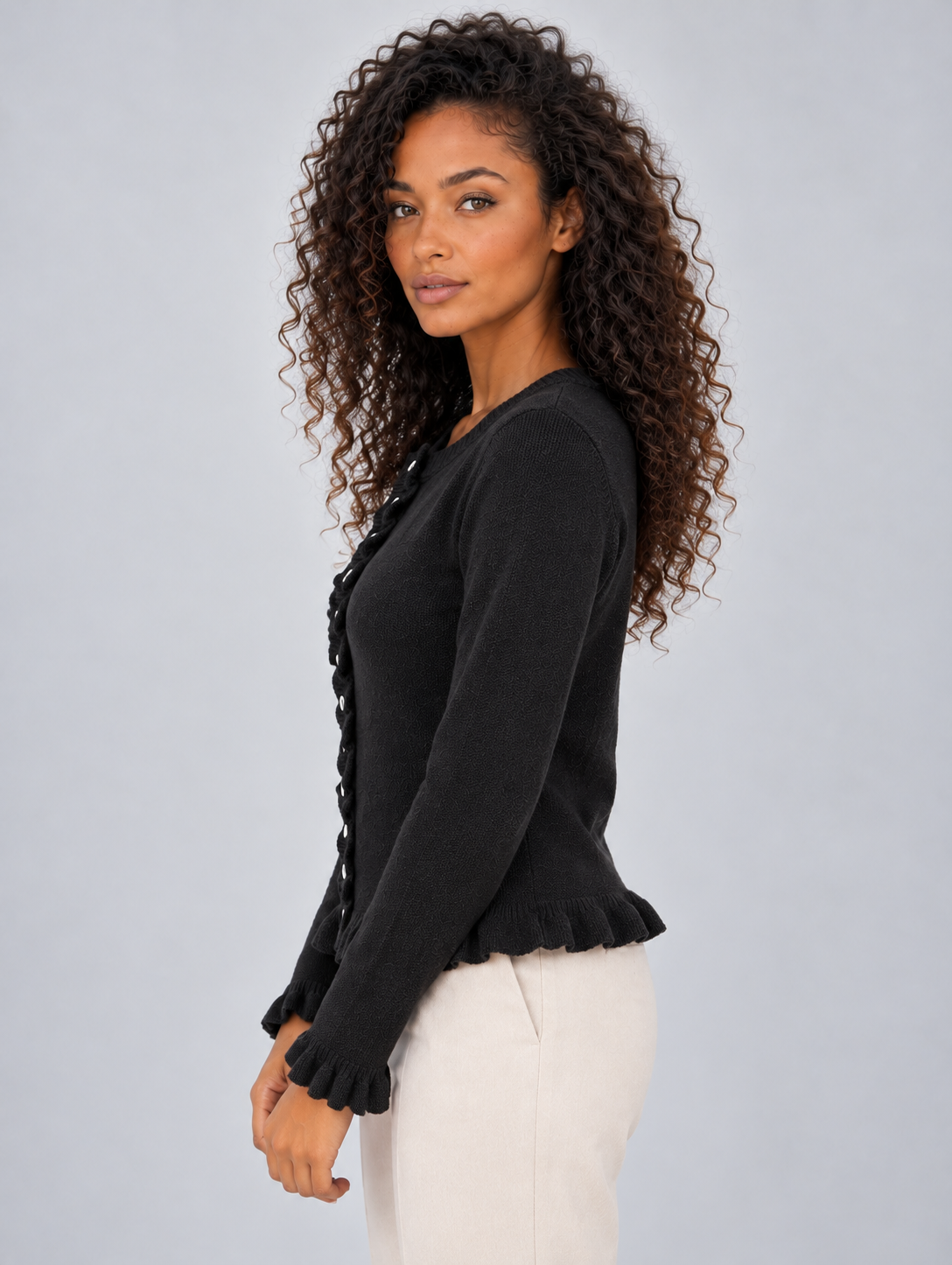 Side profile of the black cardigan showing its neat waist-length silhouette and flared ruffle hem.