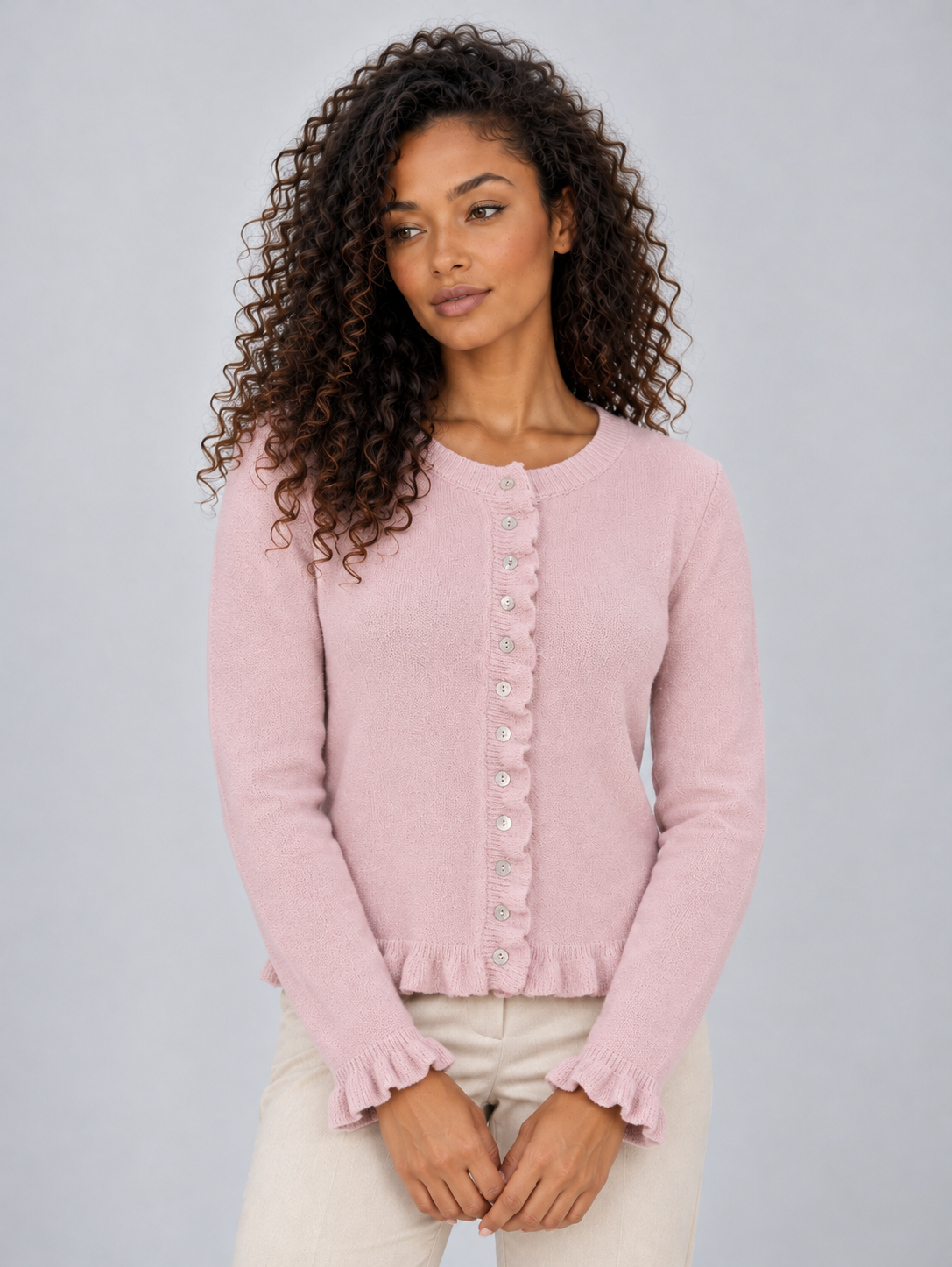 Pink button-front cardigan with a round neckline and soft ruffle detailing framing the hem and sleeve cuffs.