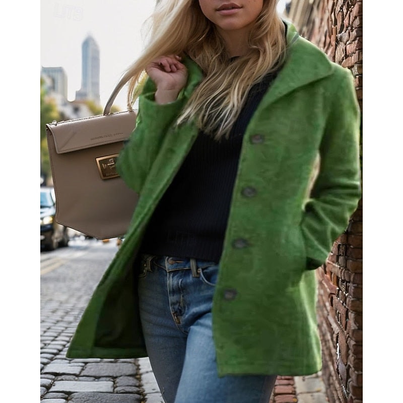 Green button-front coat with a notched collar and front pockets layered over a dark top beside a brick wall.