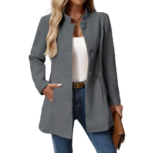 Gray button-front collarless longline coat styled open over a white top and jeans, with one hand in a side pocket.