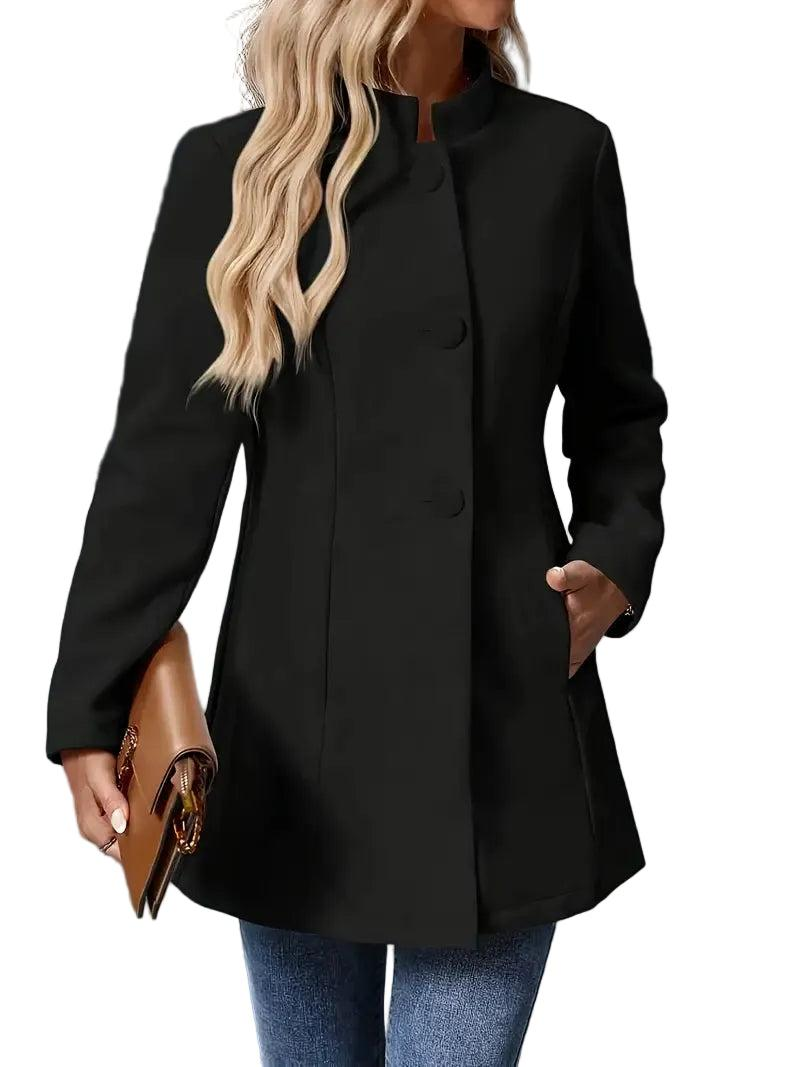 Black collarless longline coat fully fastened over jeans, showing its clean front and hands tucked into the side pockets.