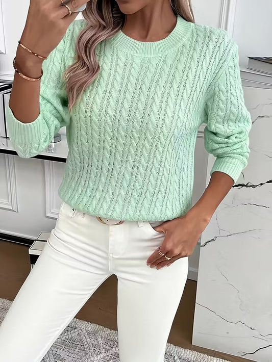 Mint green cable knit crew neck sweater styled with white jeans, shown from the front with one hand raised.