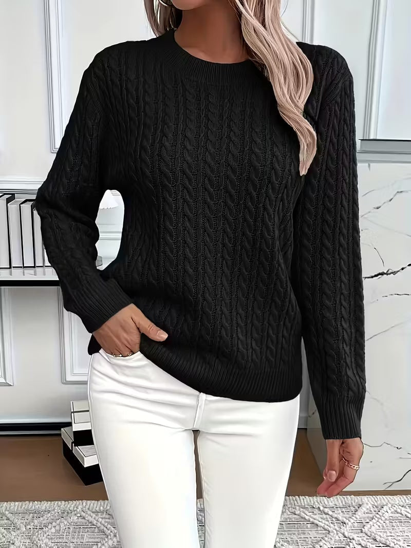 Black cable knit crew neck sweater with long sleeves and pronounced vertical texture, styled with white jeans.