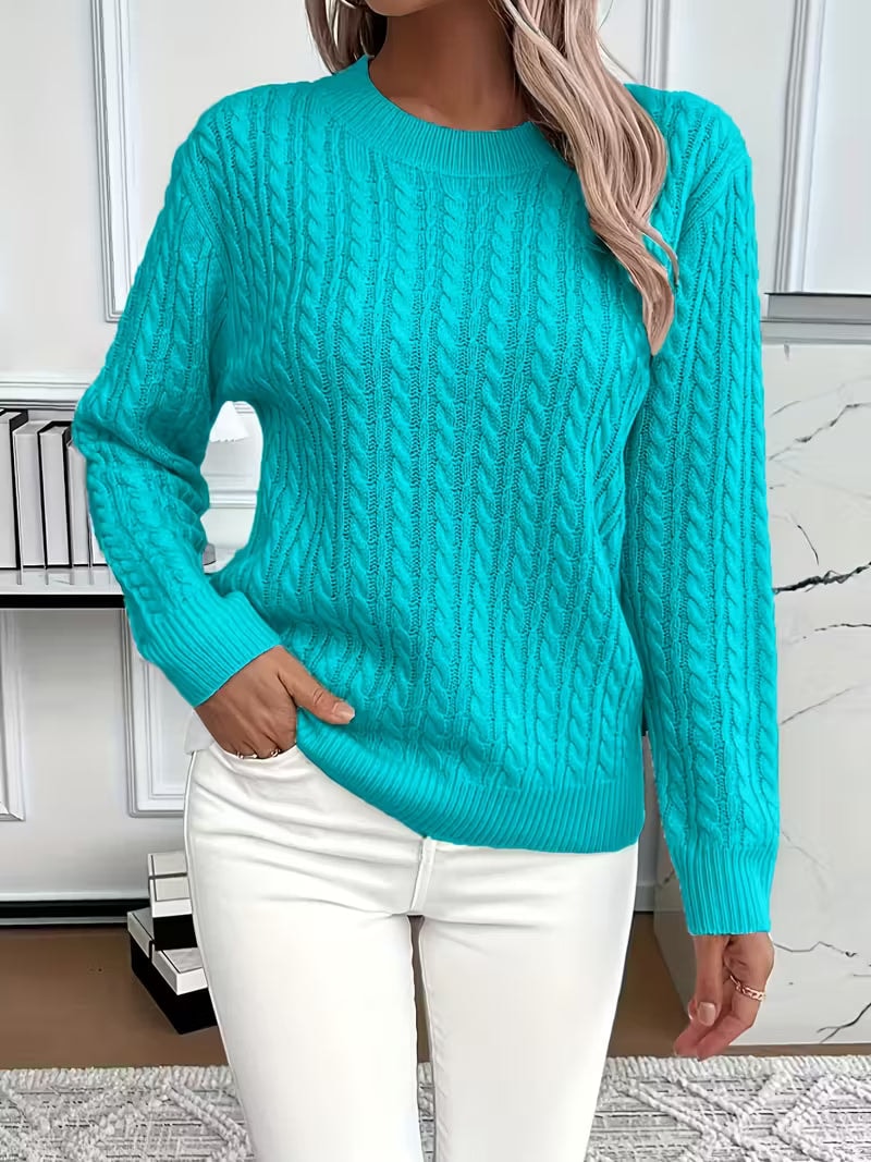Bright turquoise cable knit crew neck sweater with long sleeves and a ribbed hem, styled with white jeans.
