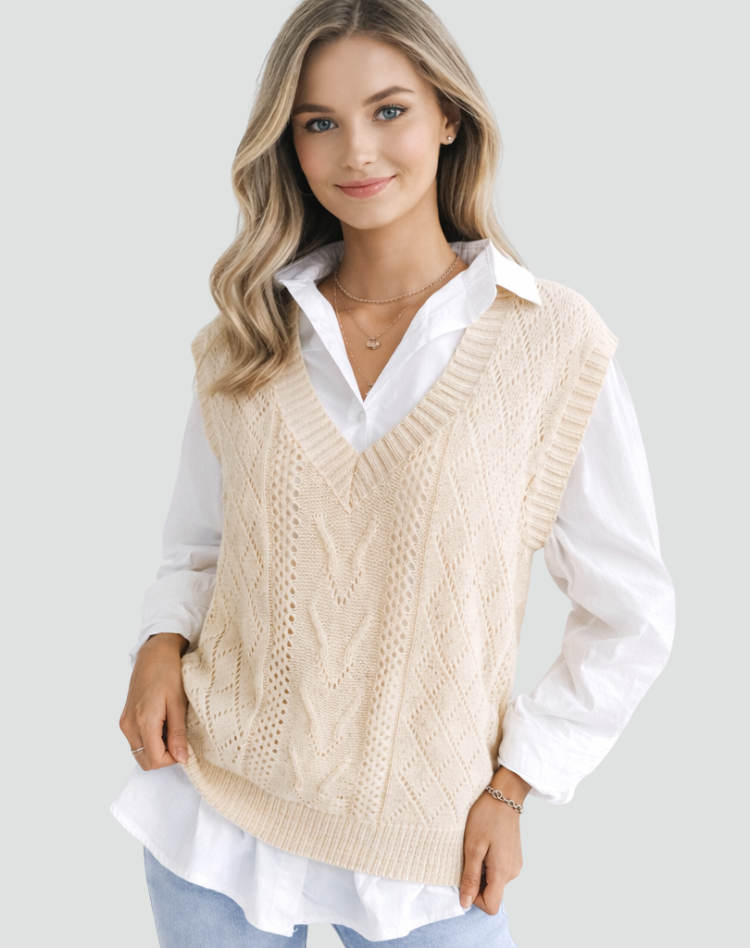 Cream cable knit V-neck sweater vest layered over a white collared shirt, shown from the front with ribbed edges and a relaxed sleeveless fit.
