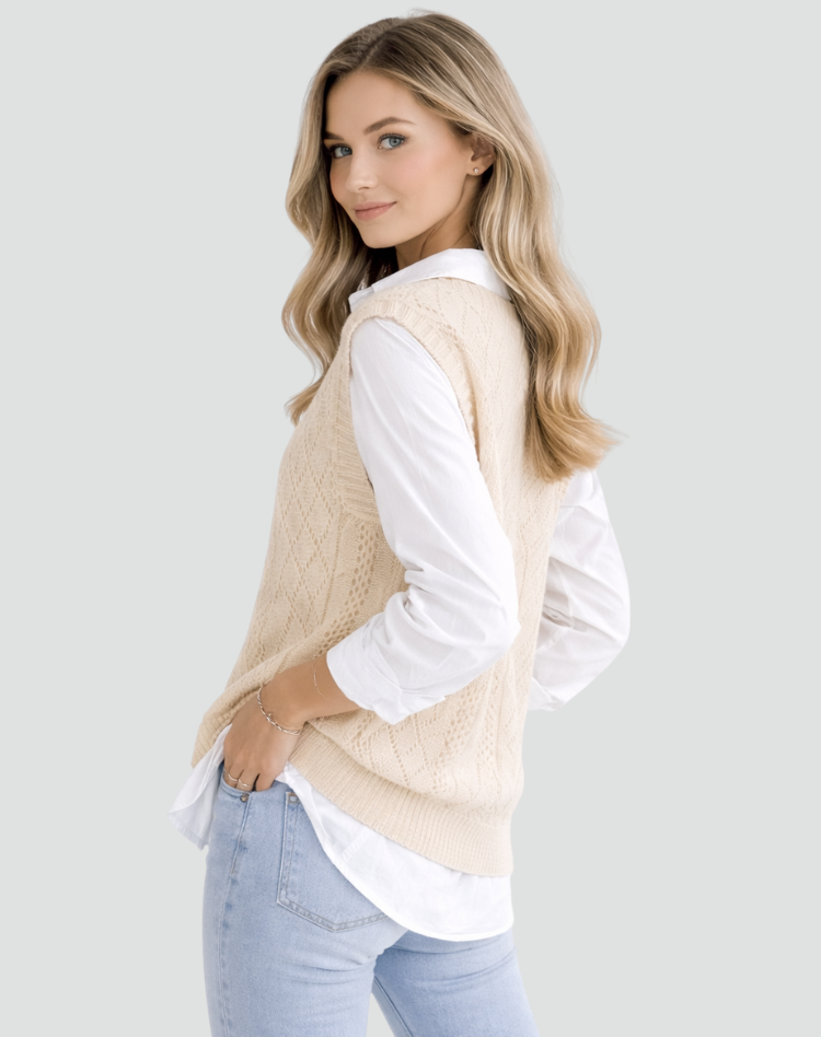 Cream cable knit sweater vest shown from a three-quarter back view, highlighting its sleeveless armholes, textured pattern, and ribbed hem over a white shirt.