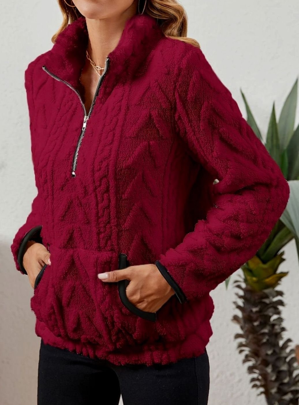 Three-quarter front view of the burgundy pullover with the quarter zip partly open and both hands tucked into the kangaroo pocket.