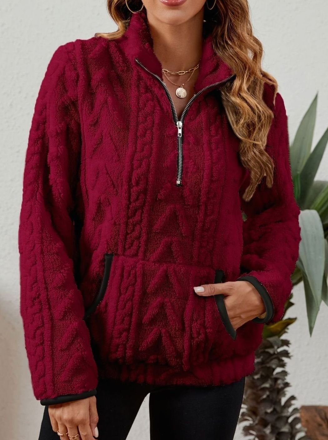 Front view of the burgundy pullover with one hand resting inside the kangaroo pocket and the contrasting sleeve-cuff trim visible.