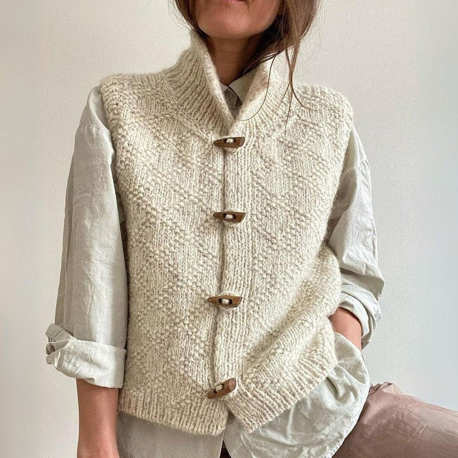 Cream chunky knit vest layered over a white shirt, shown fastened with four toggle closures and a high neckline.