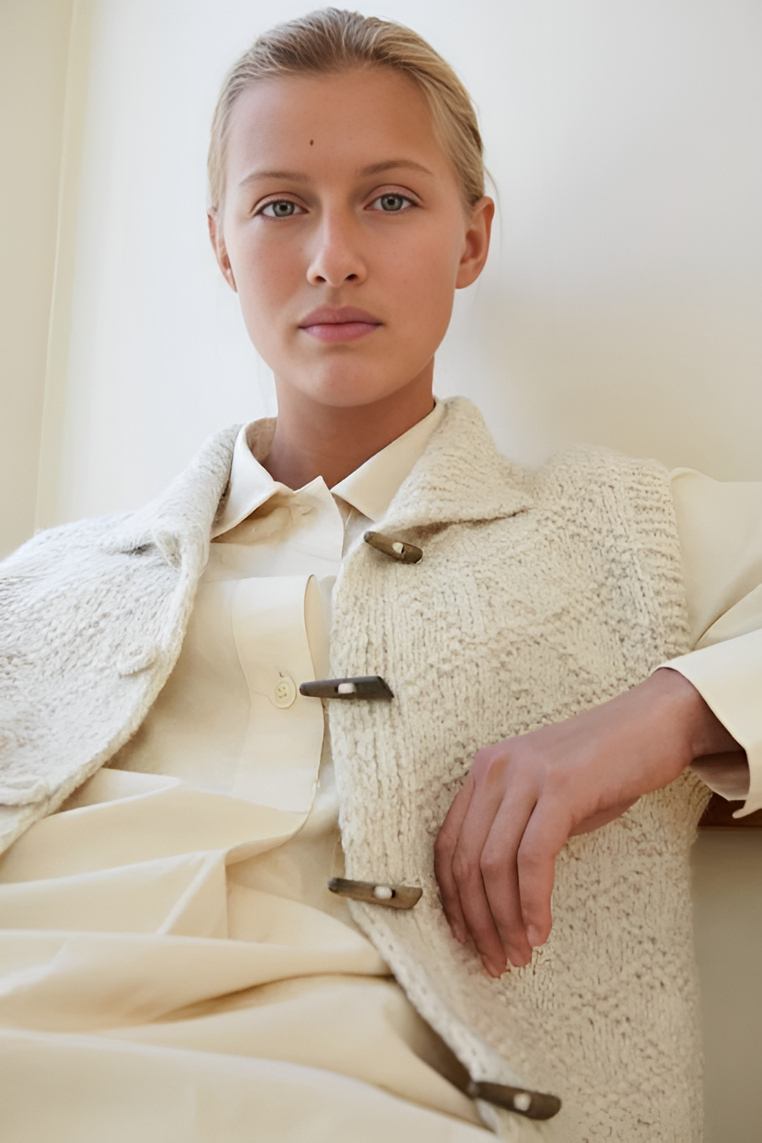 Cream textured toggle vest styled over a light blouse, showing the high neck, four front closures, and relaxed layered fit.