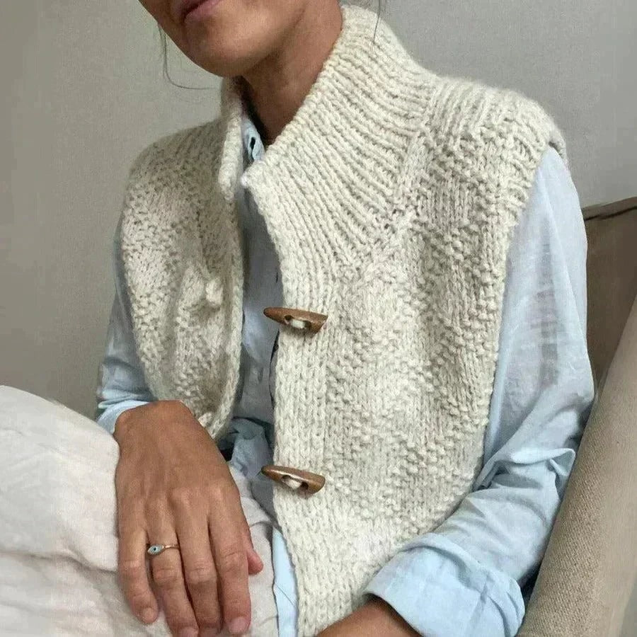 Cream sleeveless knit vest worn over a pale blue shirt, with the high neck and two visible wooden toggles shown at an angle.