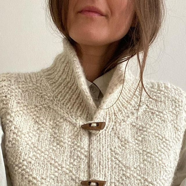 Close view of the vest’s high ribbed neckline, textured knit surface, and upper wooden toggle closures over a collared shirt.