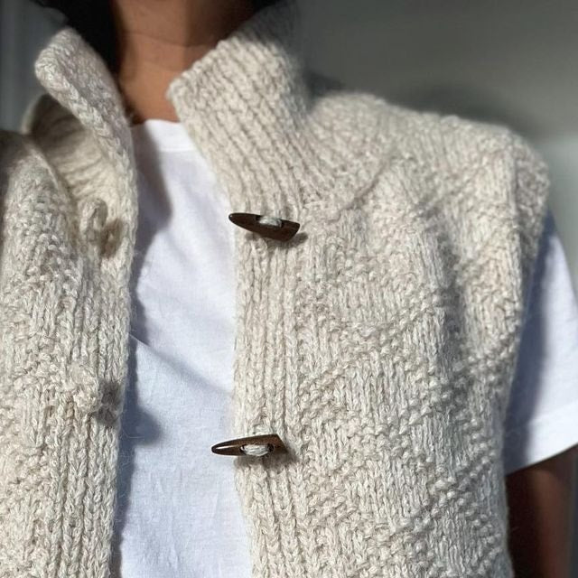 Detailed view of the vest front worn over a white T-shirt, highlighting the raised knit texture and two central toggle fastenings.