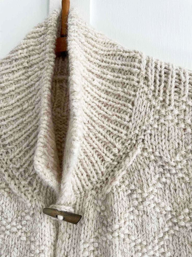 Close-up of the vest’s high ribbed collar and upper toggle fastening, with the textured knit pattern visible across the shoulder.