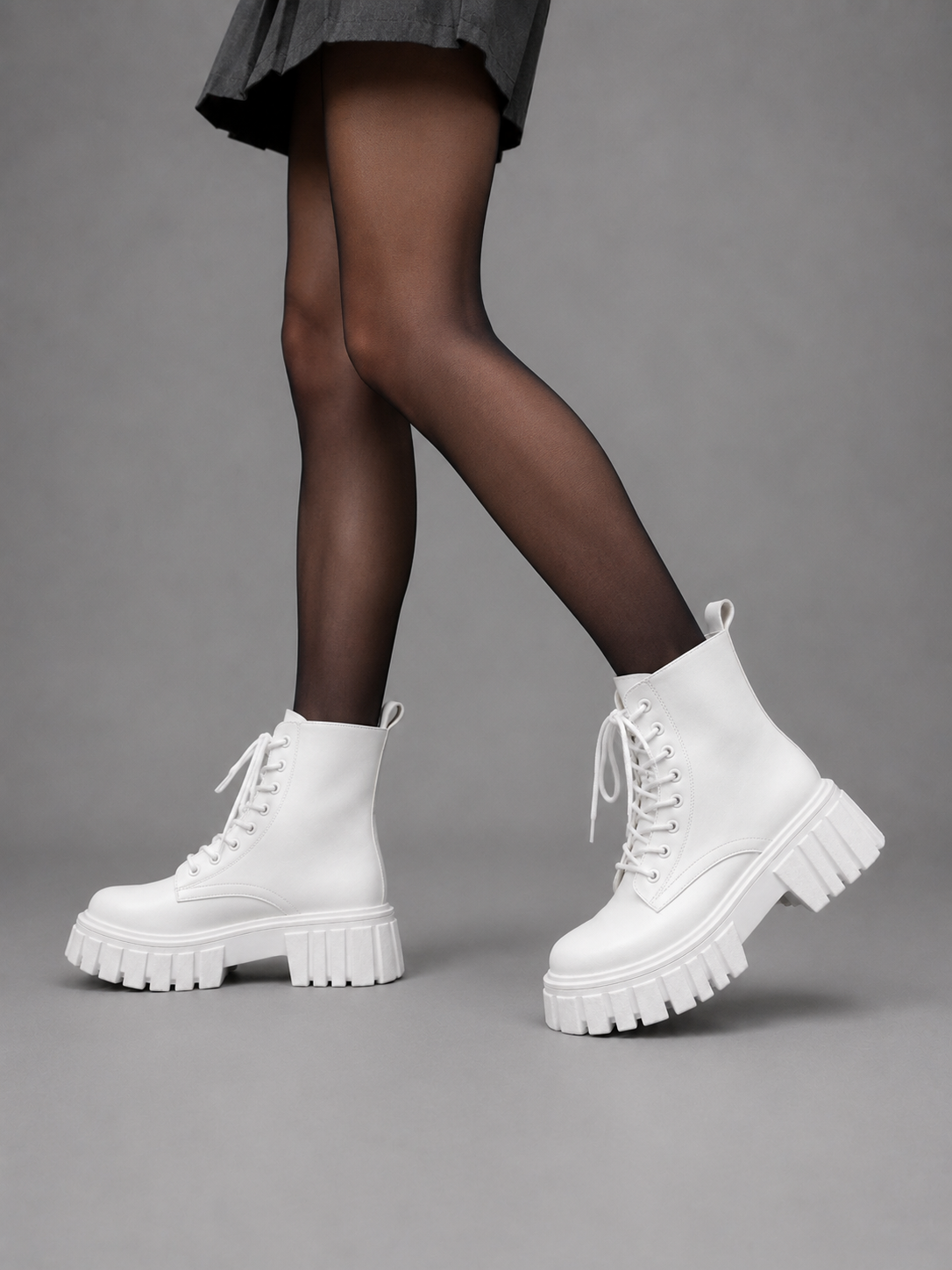 Model wearing white platform combat boots with crossed legs, showing the lace-up fronts, ankle height, and bold treaded soles.