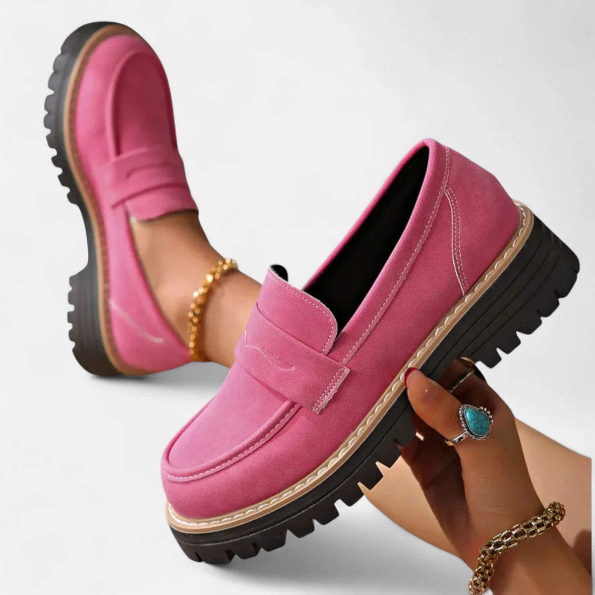 Pink penny loafers shown with one shoe held in hand, highlighting the rounded toe, layered sole, and deep tread.