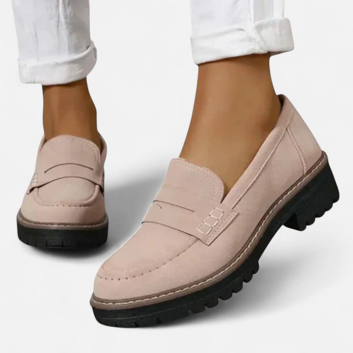 Light beige penny loafers worn with white trousers, presenting a close three-quarter view of the rounded toe and welt detail.