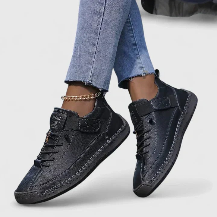Black low-top sneakers with laces and adjustable ankle straps shown on crossed feet.