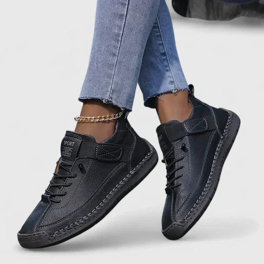 Black low-top sneakers with laces and adjustable ankle straps shown on crossed feet.
