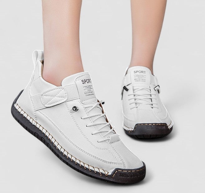 White sneakers worn on feet, with lace-up fronts, adjustable straps, and contrasting dark outsoles.
