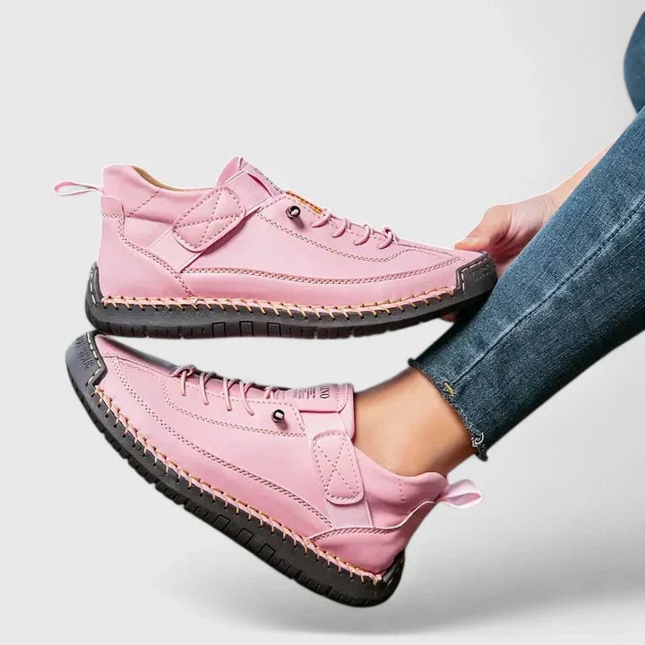 Pink sneakers shown in profile, highlighting the adjustable straps, laces, pull tabs, and black outsoles.