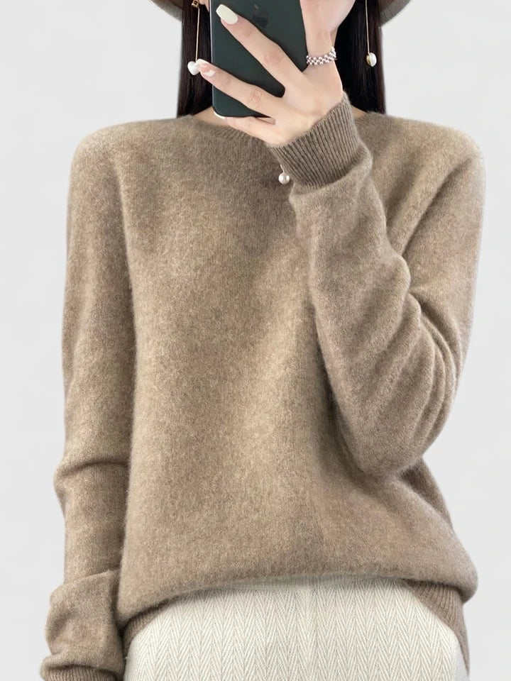 Taupe crew neck sweater against a plain background, with ribbed cuffs and a relaxed hem over light trousers.