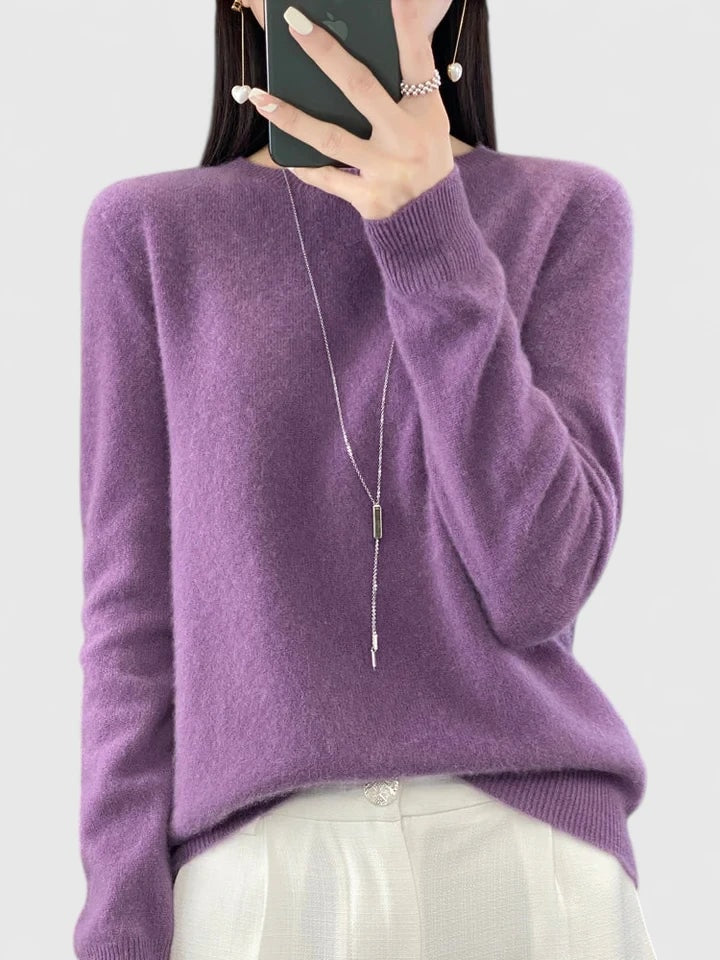 Purple crew neck sweater against a plain background, styled with a long pendant necklace and light trousers.
