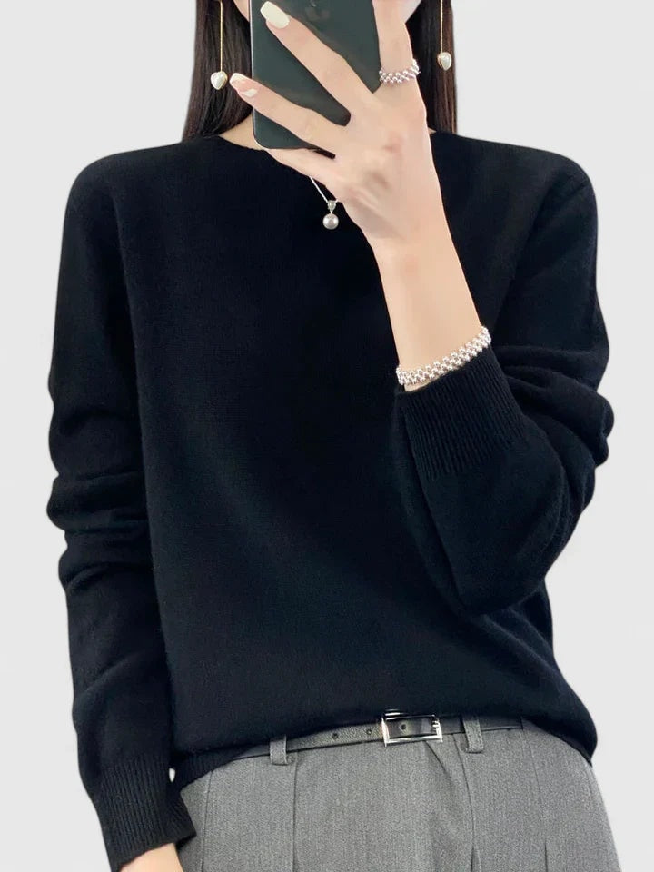 Black crew neck sweater against a plain background, paired with gray tailored trousers and a visible belt.