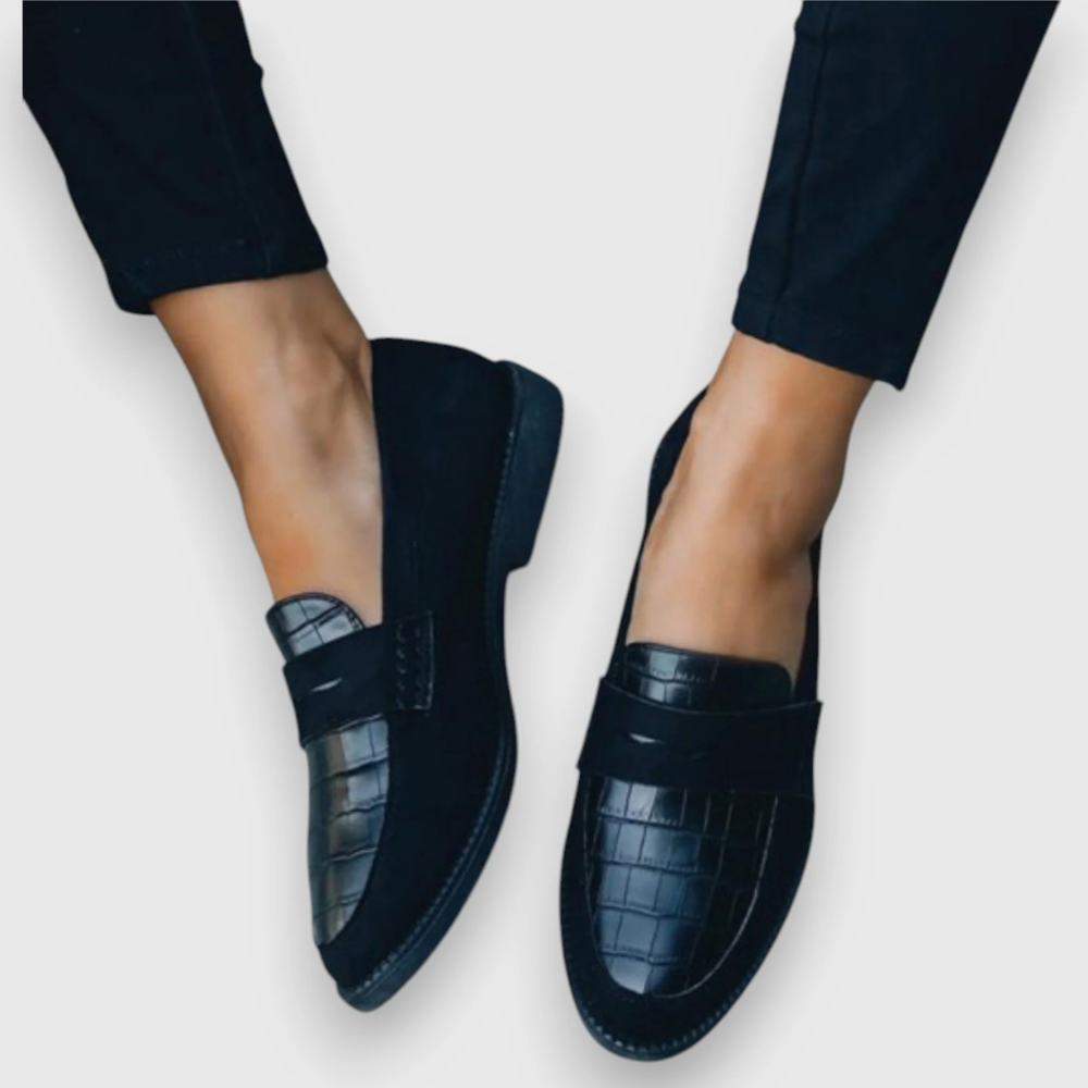 Pair of black croc-embossed penny loafers shown from an angled view, highlighting the textured front panels and low-profile soles.