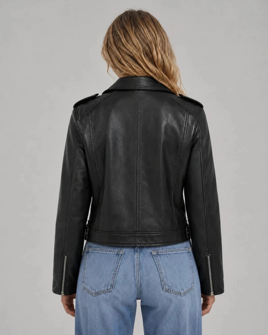 Back view of the black cropped biker jacket showing its fitted cropped shape, long sleeves, shoulder epaulettes, and back seams.