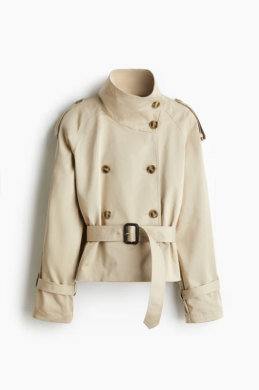Front view of the cropped beige double-breasted trench coat with stand collar, belted waist, shoulder epaulettes, and cuff straps.