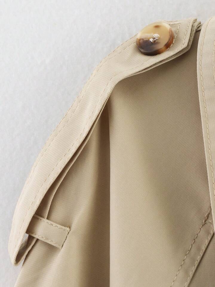 Detail view of a beige trench coat shoulder epaulette with its button and stitched strap construction.