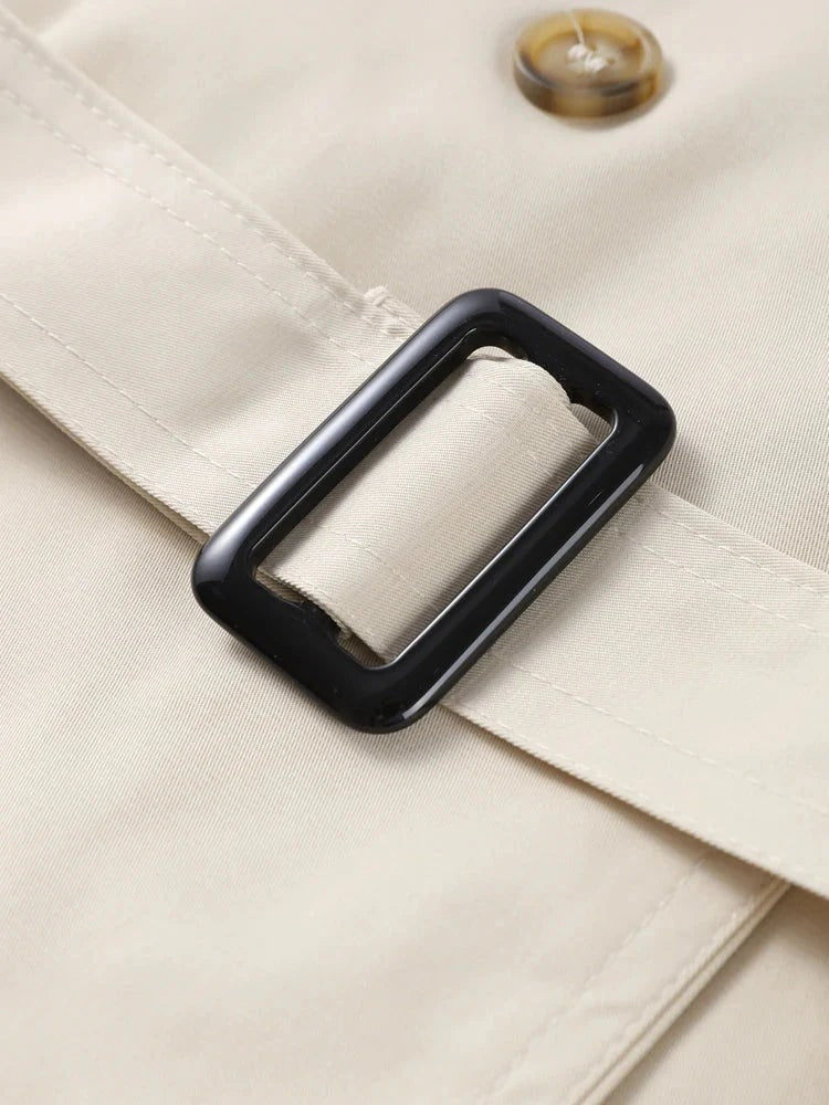 Close-up detail of the trench coat waist belt passing through a dark rectangular buckle beside a front button.