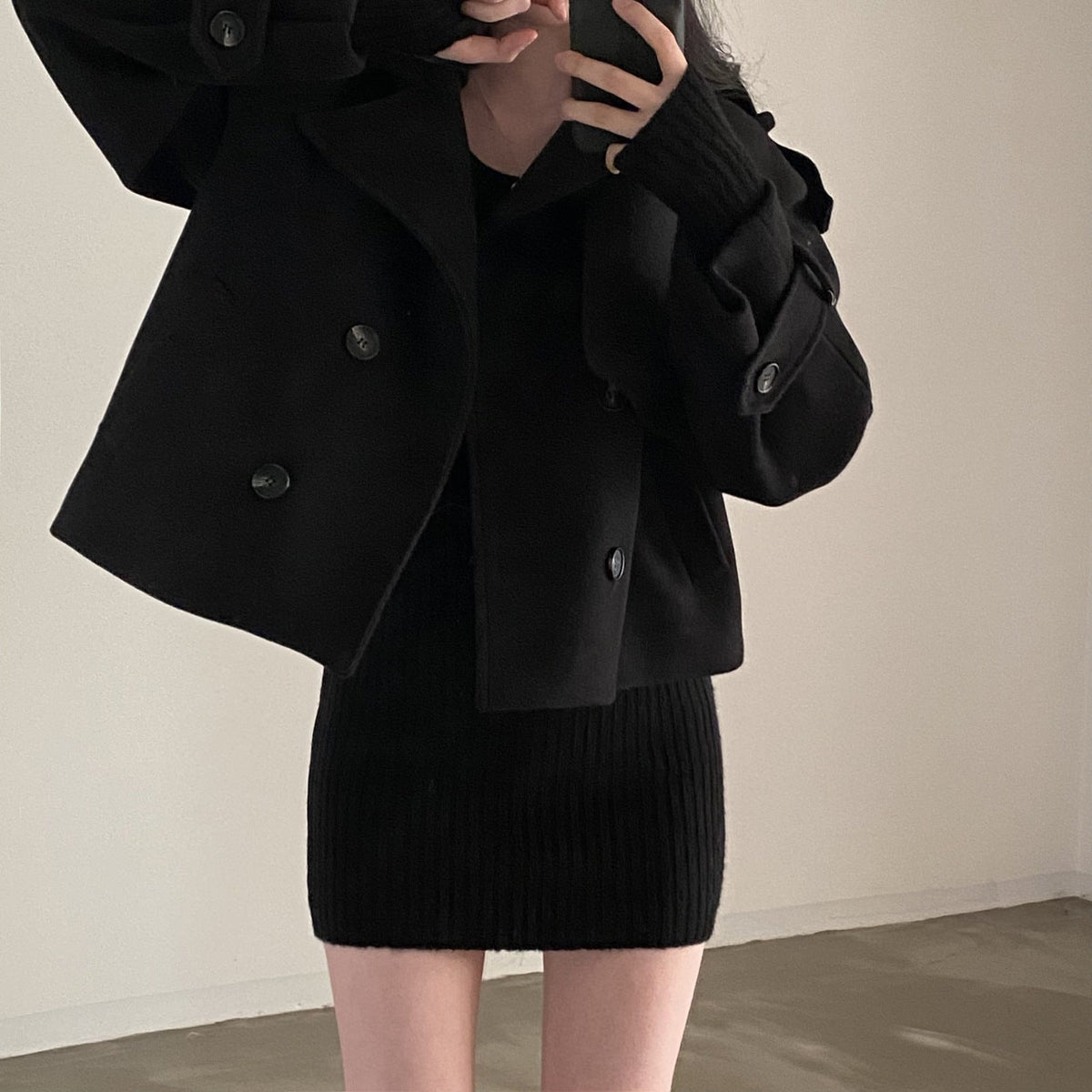 Black cropped double-breasted peacoat styled with a black ribbed dress, featuring a wide notched collar, contrasting dark buttons, and raised tabbed cuffs.