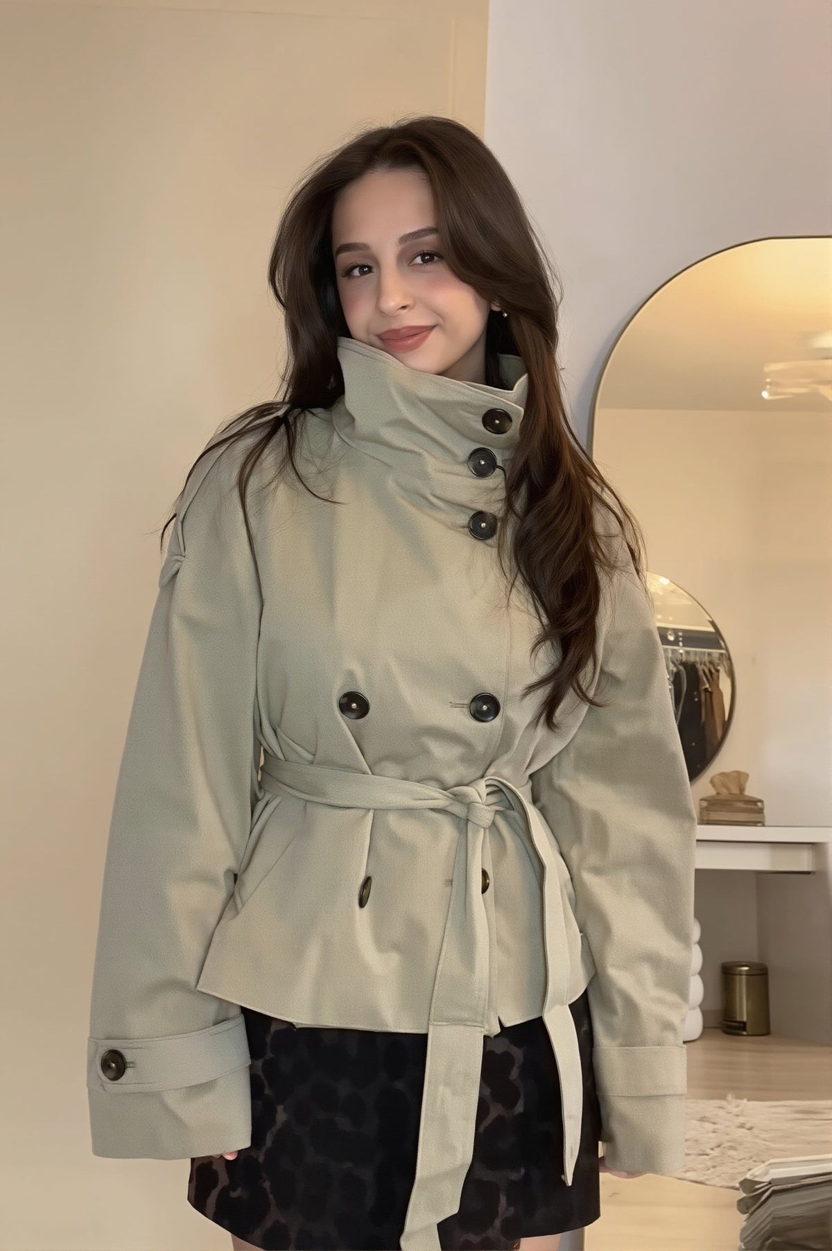 Cropped double-breasted trench jacket paired with a short skirt, featuring a high collar, waist tie, shoulder epaulettes, and wide cuff tabs.