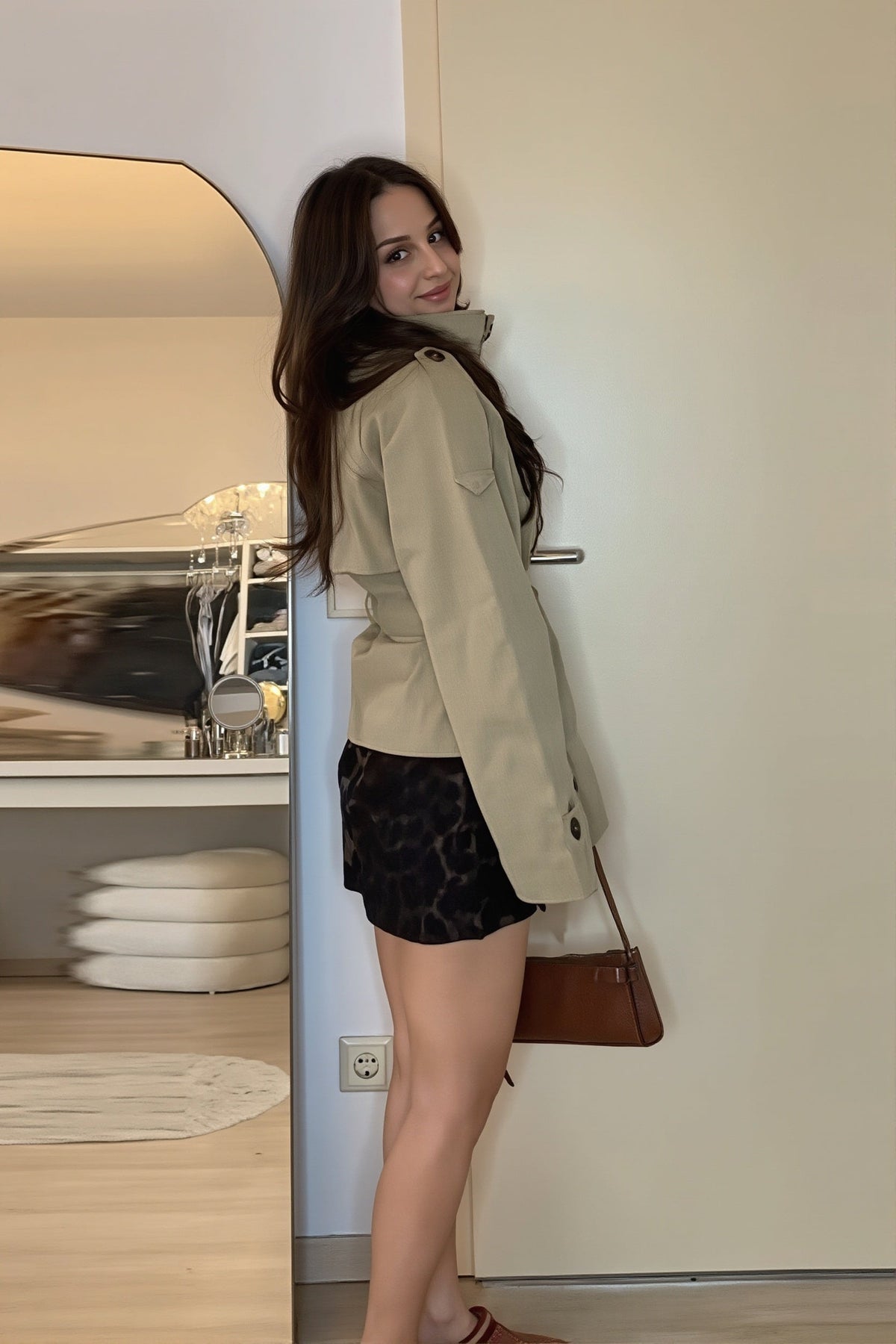Side profile of the belted cropped trench jacket, showing its short structured silhouette, raised collar, long sleeve, and back waist shaping.
