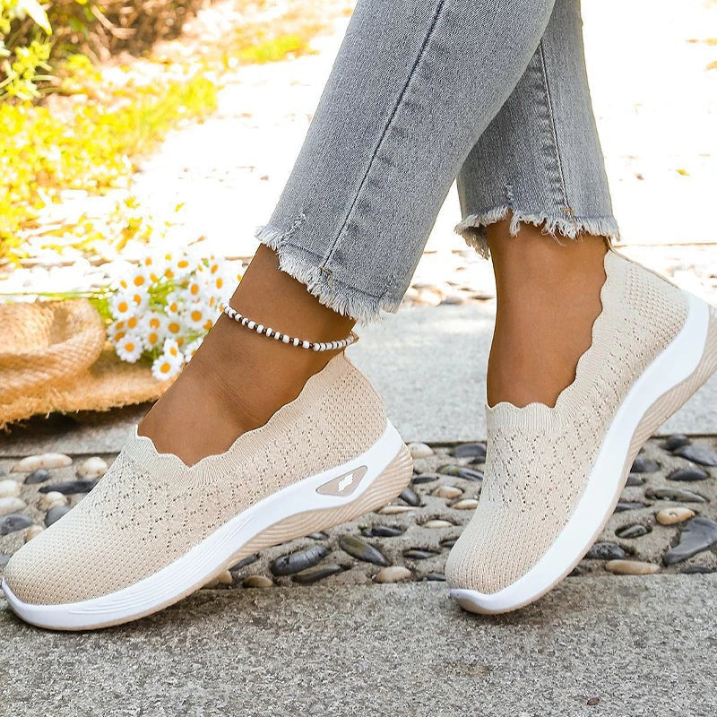 Close view of beige knit slip-on shoes in motion, showing the scalloped openings and textured cushioned soles.