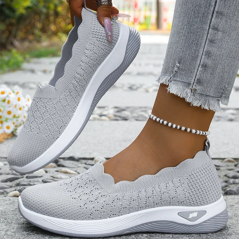 Gray knit slip-on walking shoes shown from the side with scalloped openings and cushioned soles.