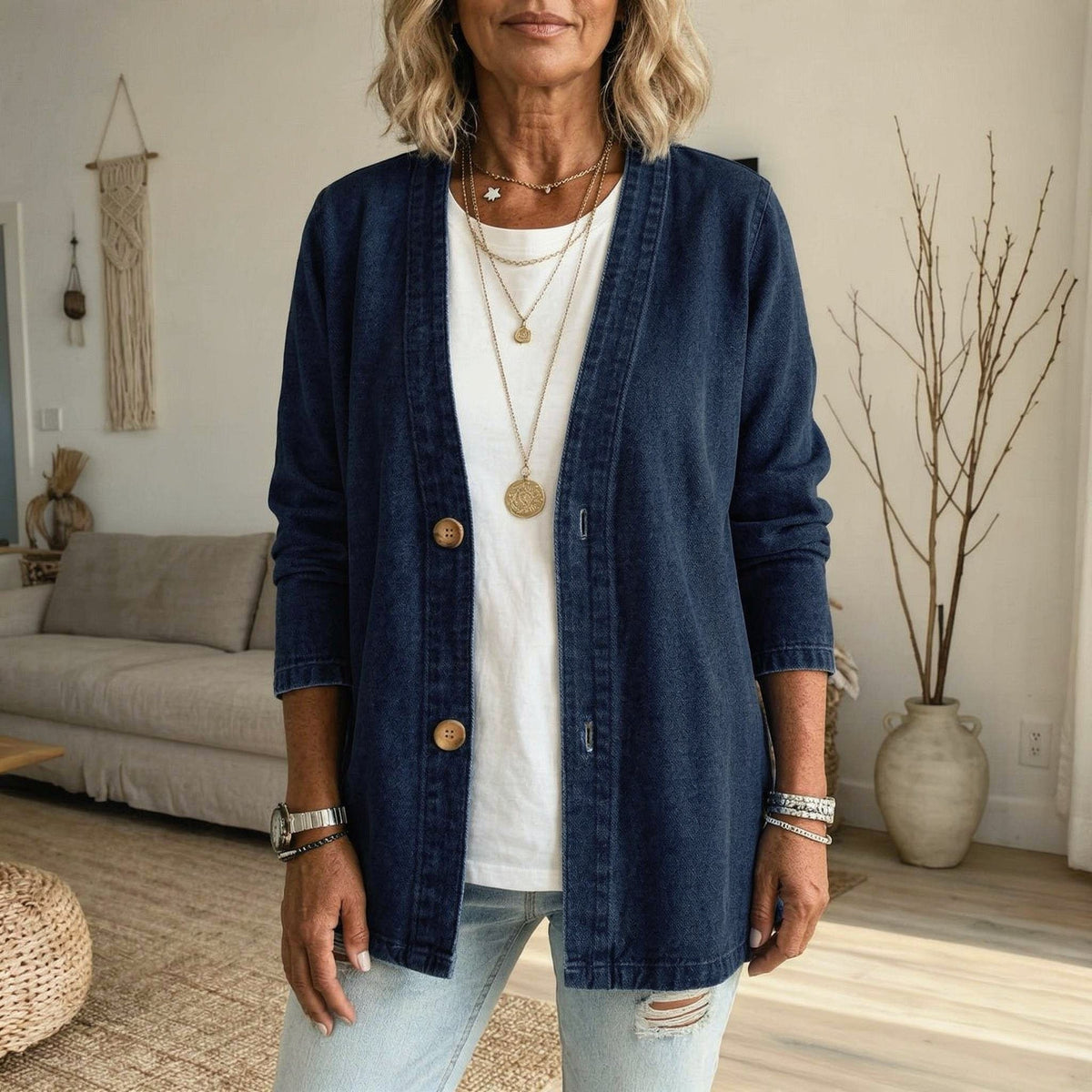 Dark blue denim jacket with a collarless V-neckline, open front, long cuffed sleeves, and visible front buttons, paired with a white top and light jeans.